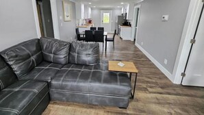 Una sala moderna con un sofá de cuero, una mesita de madera y un comedor al fondo.