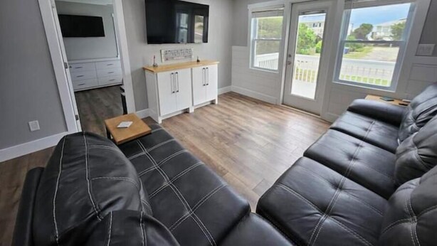 Una sala de estar moderna con un sofá de cuero negro, una mesa de centro de madera, un mueble blanco y un televisor de pantalla plana.