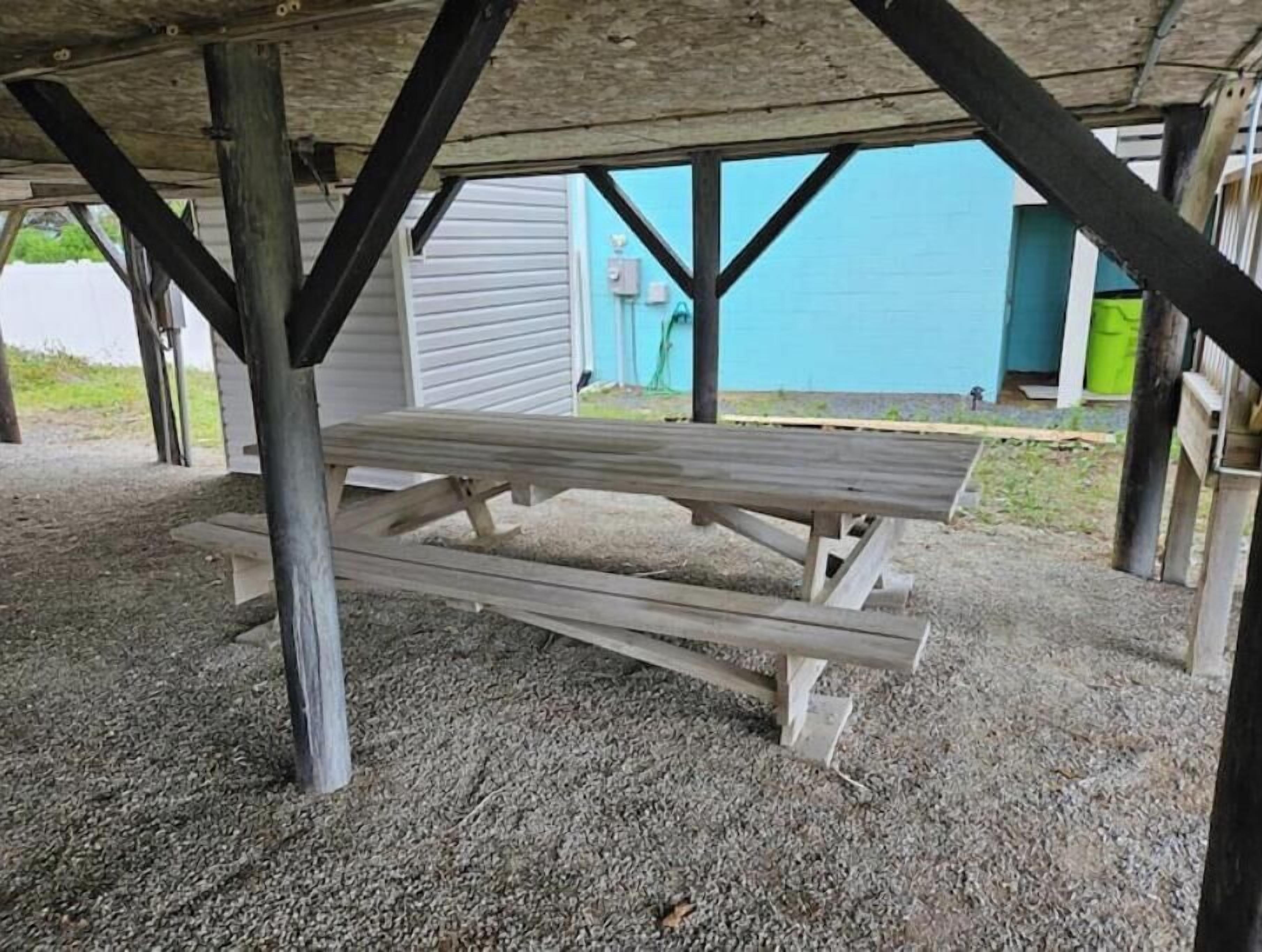 Una mesa de picnic bajo una estructura de madera con soportes metálicos.