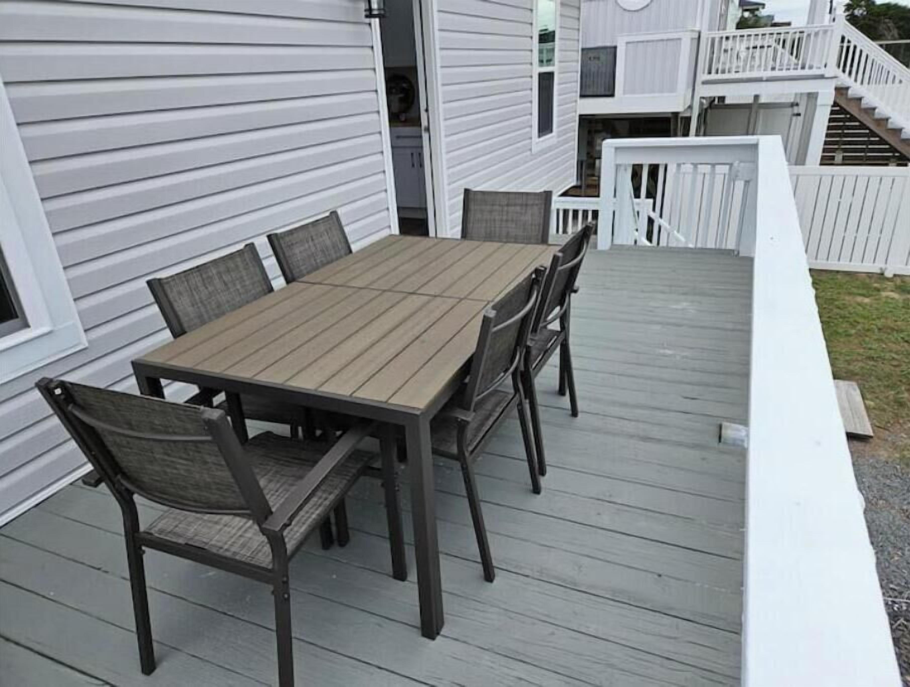 Eine Holzterrasse mit Tisch und Stühlen, weißen Geländern und einem Haus im Hintergrund.
