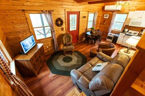 Un intérieur de chalet chaleureux, avec un revêtement mural en bois, un téléviseur, un coin repas et une cuisine.