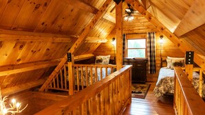 A cozy attic bedroom with a wooden staircase, a bed with floral bedding, and a window with curtains. - Log Cabin Near Bangor and Acadia National Park (Winterport)