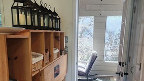 Una stanza con scaffali in legno, una porta che dà all'esterno e vista su una sedia all'aperto.