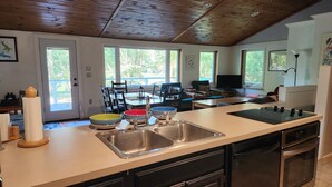 Una cucina con un'isola grande, lavello in acciaio inossidabile e lavastoviglie. Diverse finestre offrono luce naturale e vista all'esterno.