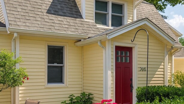 A two-story house with a red door, beige siding, and a small porch with a chair. - Stay in a centrally located home, 1.5 miles from downtown Ann Arbor. (Ann Arbor)