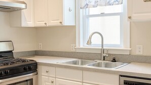 A modern kitchen with white cabinets, a stainless steel stove, a dishwasher, and a window with a floral curtain. - Stay in a centrally located home, 1.5 miles from downtown Ann Arbor. (Ann Arbor)