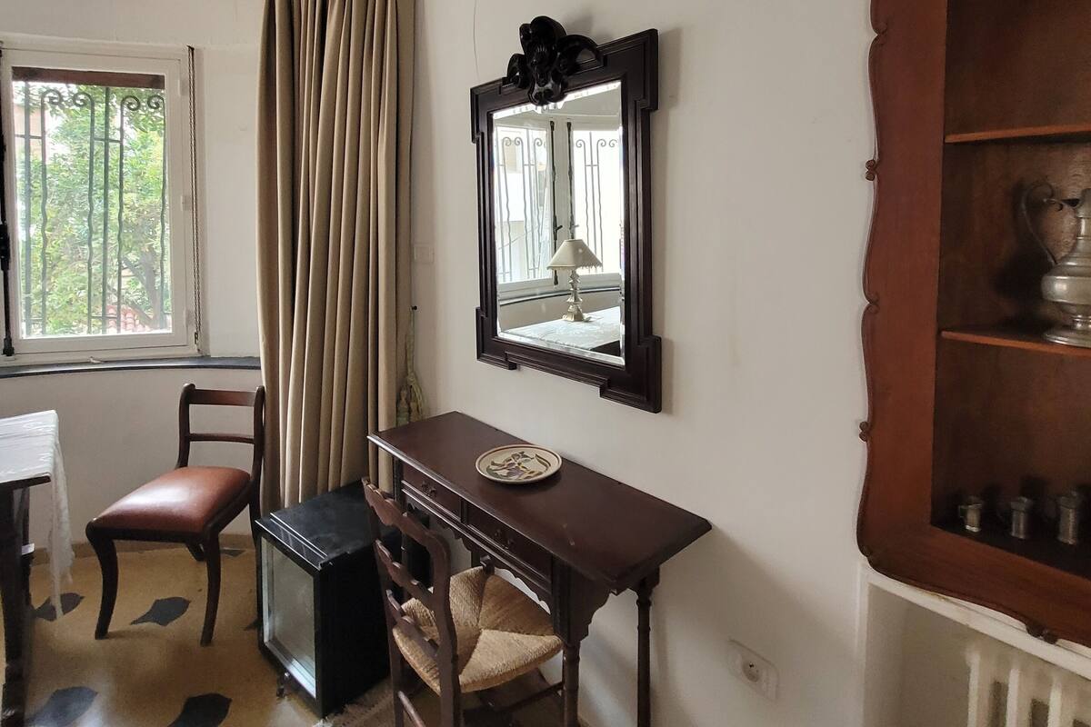 Une pièce avec un bureau en bois, une chaise, un grand miroir et un radiateur.