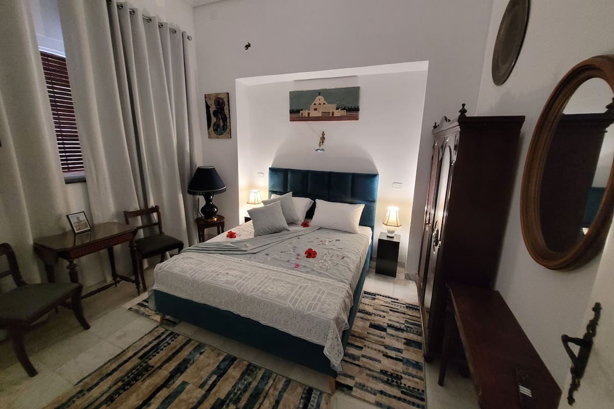 Une chambre d’hôtel comprenant un lit, des lampes de chevet, un bureau, une chaise, une commode, un miroir et une fenêtre avec des rideaux.