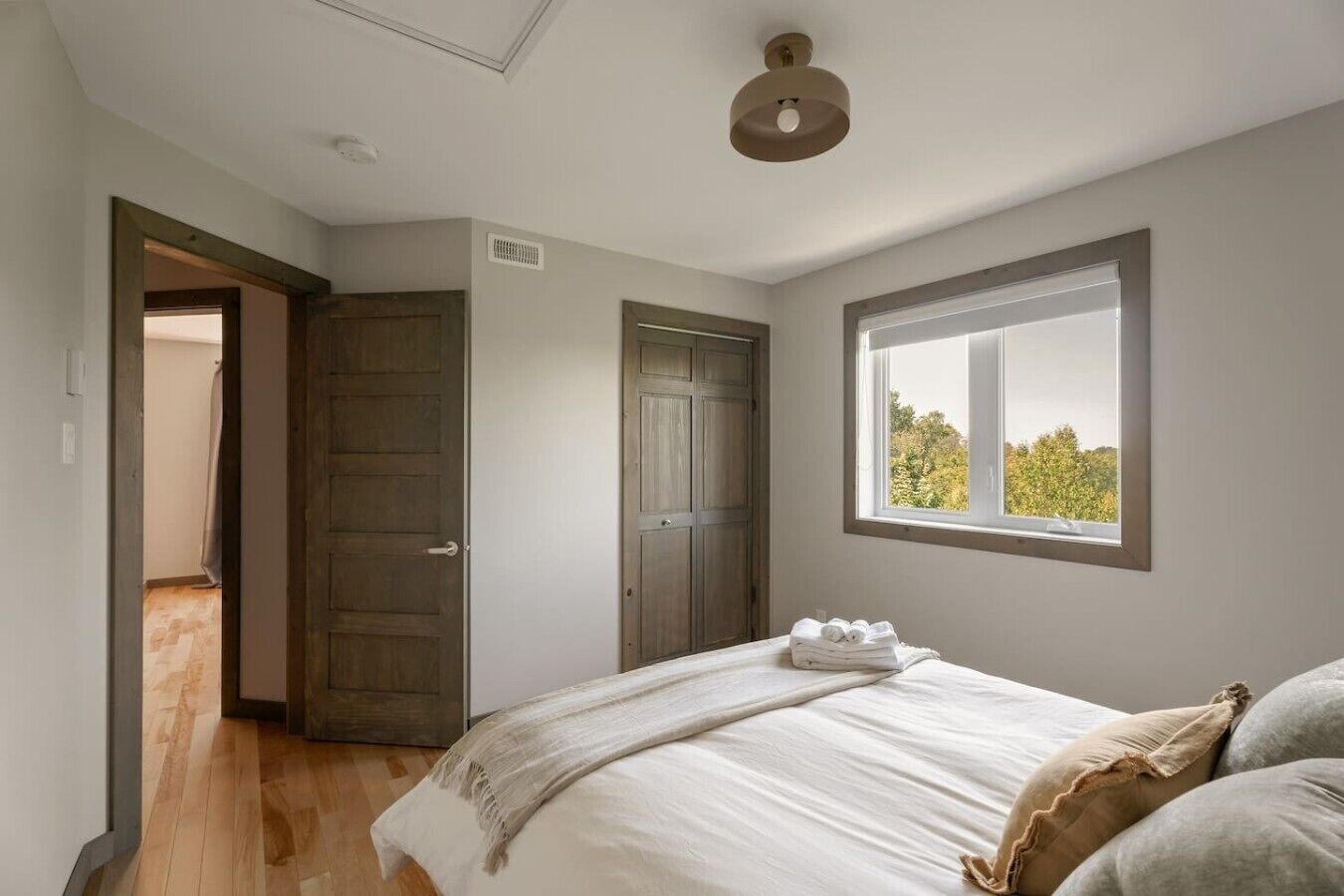 Une chambre à coucher avec un lit, une fenêtre donnant sur un paysage agréable, une porte et un luminaire au plafond.