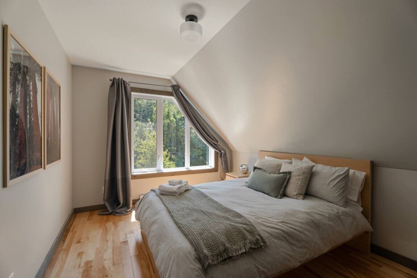 Une chambre avec un grand lit, une fenêtre avec des rideaux et un tableau accroché au mur.