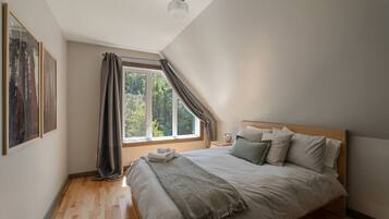 Ein Schlafzimmer mit einem großen Bett, einem Fenster mit Vorhängen und einem Gemälde an der Wand.