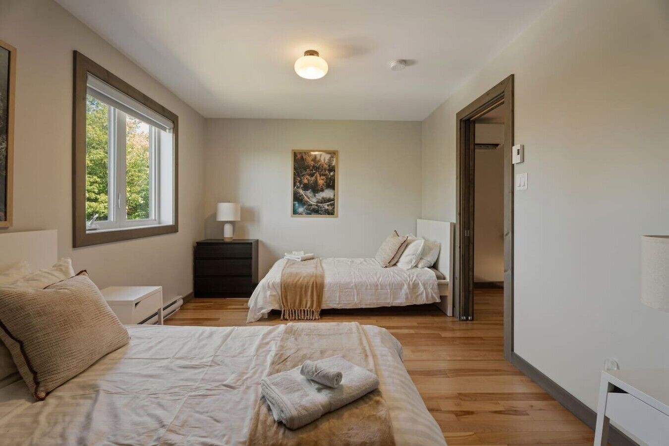 A bedroom with two beds, a nightstand, a lamp, and a painting on the wall.
