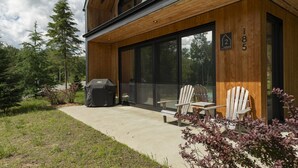 Ein modernes Gebäude mit Holzfassade, einer Grillkota und zwei Adirondack-Stühlen.