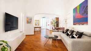 Un salón moderno con un televisor de pantalla plana, un sofá con cojines estampados, una mesa de centro y un cuadro abstracto de gran tamaño.