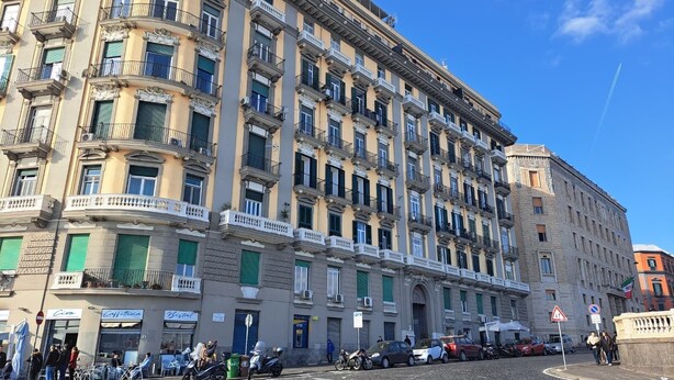 Un edificio de varios pisos con balcones, una calle adoquinada y un cielo azul despejado.