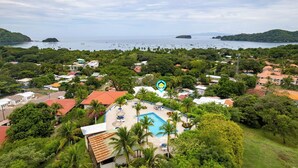 A coastal area with a swimming pool surrounded by lush greenery and residential buildings. - Modern Top-Floor Condo with Panoramic Views and Community Pool (Sardinal)