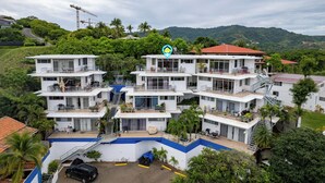 A multi-story hotel with balconies, a swimming pool, and a view of the surrounding greenery. - Modern Top-Floor Condo with Panoramic Views and Community Pool (Sardinal)