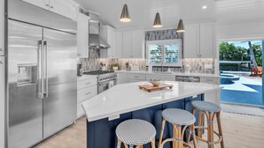 A modern kitchen with stainless steel appliances, a large island with bar stools, and a view of a swimming pool.