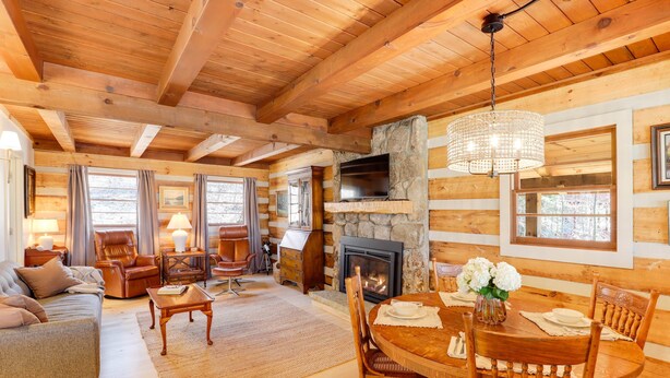 Un acogedor interior de cabaña de madera con chimenea, mesa de comedor de madera y asientos cómodos.