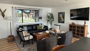 A modern living room with a black sofa, two armchairs, a coffee table, and a TV mounted on the wall. - Modern Upscale Hermiston Home • Pet-Friendly • Private Fenced Yard (Hermiston)