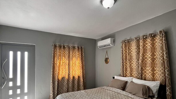 A bedroom with a bed, curtains, an air conditioning unit, and a door with a handle.