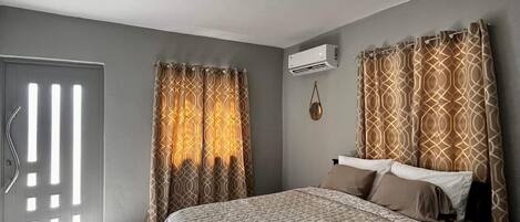 A bedroom with a bed, curtains, an air conditioning unit, and a door with a handle.