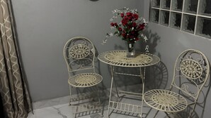 A corner room with a marble floor, two metal chairs, a small table, a vase with flowers, and two wall decorations.