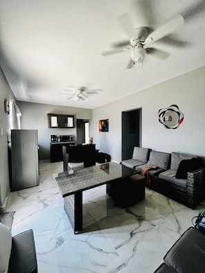 A living room with a sofa, a coffee table, a dining table, a kitchen area, and a ceiling fan. - Delightful 3-bedroom house with AC in charming Rincón (Rincón)