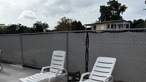 Two white lounge chairs on a concrete patio with a chain-link fence in the background.