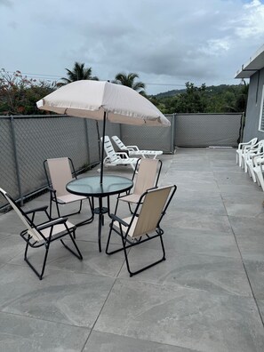 An outdoor patio with a round table and chairs, a large umbrella, and a chain-link fence.