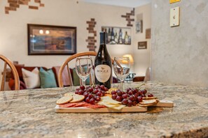 Een eettafel met een fles BOGF FAMILY CALIFORNIA wijn, twee wijnglazen en diverse snacks, waaronder druiven, crackers en kaas.