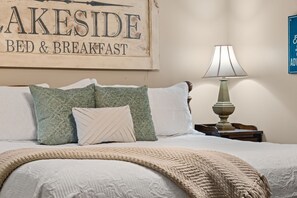 Un lit avec une tête de lit, des oreillers et une lampe de chevet, dans une chambre dont le mur porte une enseigne indiquant « AKESIDE BED & BREAKFAST ».