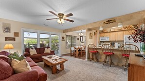 A spacious living room with a sofa, coffee table, and a dining area with wooden chairs and a kitchen in the background.