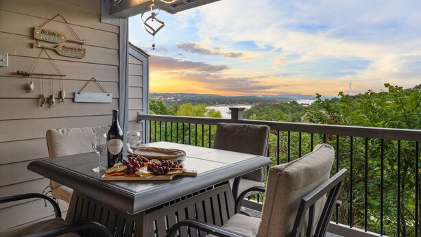 A dining area with a table set for two, featuring a bottle of wine, glasses, and a cheese board with grapes.