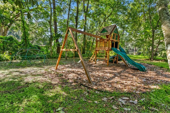 Ein Spielplatz mit Schaukel und Rutsche in einem bewaldeten Park.