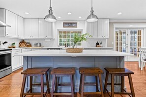 A modern kitchen with white cabinetry, a large island with stools, pendant lighting, and a view to the outside. - 4/3 with pool NW Gainesville (Gainesville)