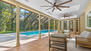 Eine geräumige Terrasse mit Pool, großen Fenstern und Deckenventilatoren.