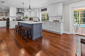 Una cocina amplia con armarios blancos, una isla grande con taburetes y vistas al exterior a través de una ventana.