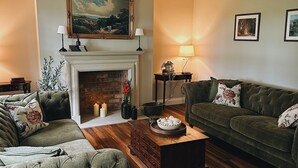 Uma sala de estar com lareira, dois sofás, uma mesa de centro e um quadro na parede.