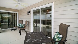 A covered patio with a table and chairs, a ceiling fan, and a sliding glass door. - Charming 3-bedroom villa walking distance to Lake Sumter Sq  Golf Cart included (The Villages)