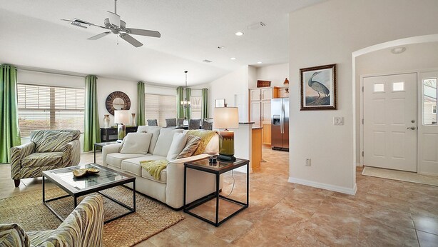 A spacious living room with a ceiling fan, a dining area, and a kitchen with a refrigerator. - Charming 3-bedroom villa walking distance to Lake Sumter Sq  Golf Cart included (The Villages)