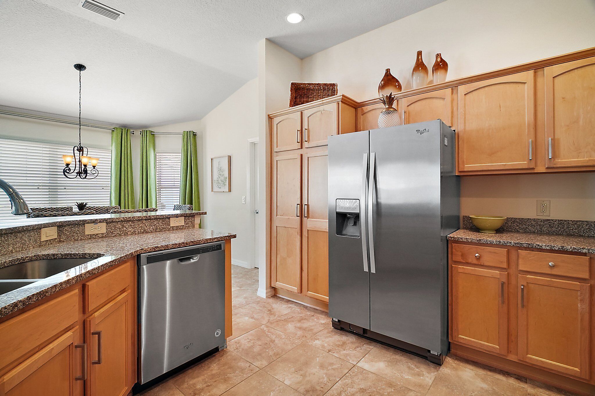 A kitchen with wooden cabinets, a stainless steel refrigerator, a dishwasher, and a granite countertop.