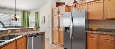 A kitchen with wooden cabinets, a stainless steel refrigerator, a dishwasher, and a granite countertop.