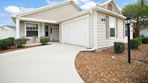 A single-story house with a garage, a covered porch, and a well-maintained front yard with gravel and small shrubs. - Charming 3-bedroom villa walking distance to Lake Sumter Sq  Golf Cart included (The Villages)