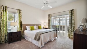 A bedroom with a bed, nightstand, lamp, and a view of the outdoors through a window. - Charming 3-bedroom villa walking distance to Lake Sumter Sq  Golf Cart included (The Villages)