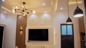 A modern living room with a flat-screen TV mounted on the wall, recessed ceiling lighting, and a wooden accent wall. - Akoka Oasis 1-Bed Near Unilag (Lagos)
