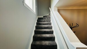 Una escalera con alfombra oscura, barandillas blancas y un pared con un sencillo adhesivo de un árbol negro.