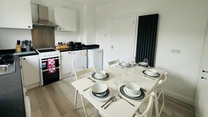 Cocina compacta con armarios blancos, estufa, lavadora y una mesa de comedor preparada para cuatro.