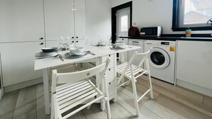 Una cocina moderna con armarios blancos, una mesa de comedor con sillas, una lavadora y una ventana con vistas.