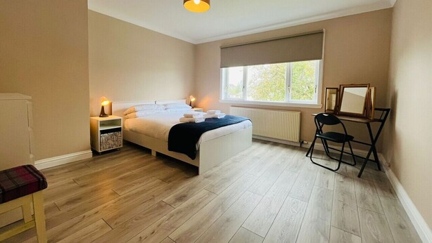 Un dormitorio con cama, mesitas de noche, una silla, un radiador y una ventana.